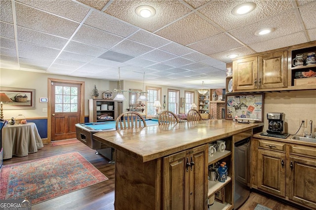 kitchen with sink, a kitchen island, hanging light fixtures, dark wood-type flooring, and billiards