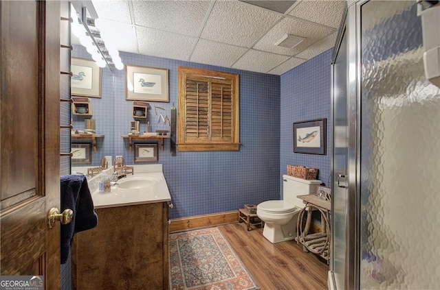 bathroom featuring toilet, a shower with shower door, wood-type flooring, a drop ceiling, and vanity