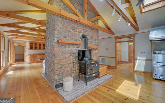 unfurnished living room featuring beamed ceiling, light hardwood / wood-style floors, high vaulted ceiling, and a wood stove