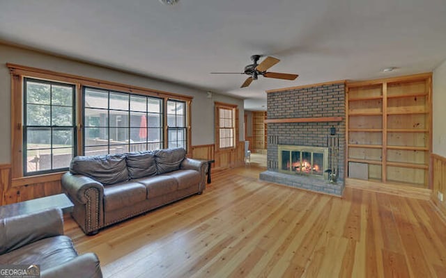 living room with a fireplace, wooden walls, light wood-type flooring, built in shelves, and ceiling fan