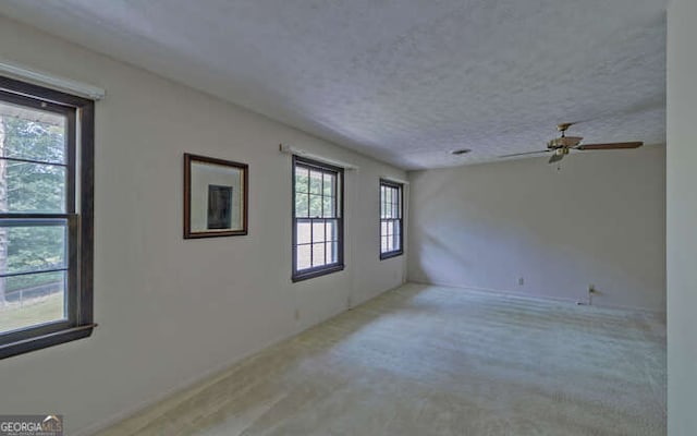 carpeted spare room with a textured ceiling, plenty of natural light, and ceiling fan