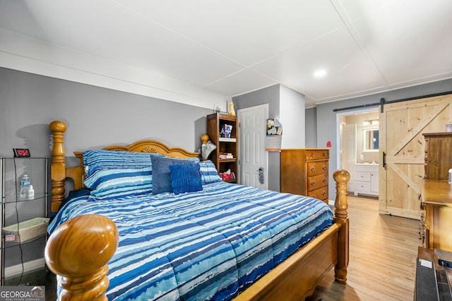 bedroom with ensuite bath, wood-type flooring, and a barn door