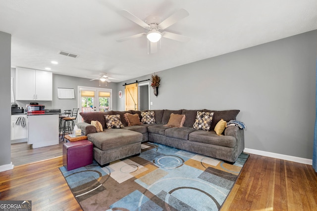 living room with a barn door, light hardwood / wood-style floors, and ceiling fan