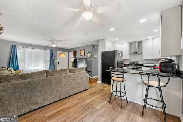 kitchen featuring wall chimney range hood, a breakfast bar area, kitchen peninsula, white cabinets, and stainless steel refrigerator