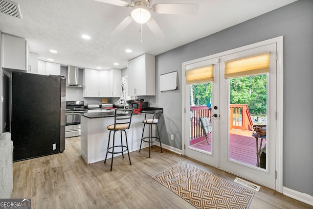 kitchen featuring appliances with stainless steel finishes, kitchen peninsula, white cabinetry, wall chimney exhaust hood, and a breakfast bar