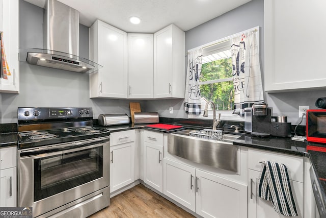 kitchen with wall chimney range hood, sink, light wood-type flooring, stainless steel electric stove, and white cabinets