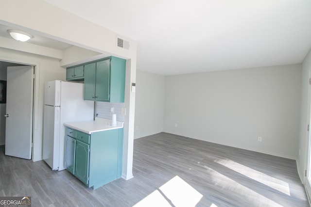 kitchen with decorative backsplash, hardwood / wood-style flooring, green cabinets, and white refrigerator