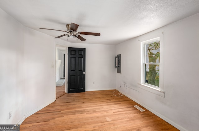 unfurnished room featuring ceiling fan, a textured ceiling, electric panel, and light hardwood / wood-style flooring