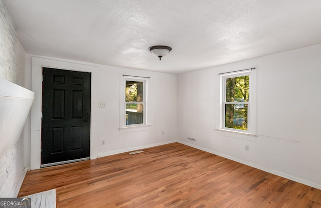 unfurnished room with light hardwood / wood-style flooring, a textured ceiling, and a wealth of natural light