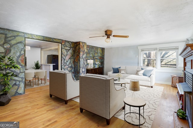 living room featuring a stone fireplace, light hardwood / wood-style floors, and ceiling fan