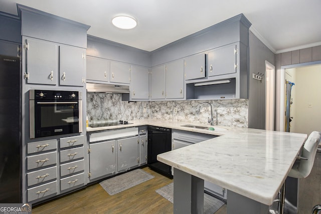 kitchen with a breakfast bar area, dark wood-type flooring, kitchen peninsula, sink, and black appliances