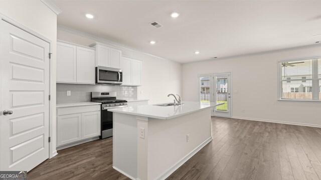kitchen with white cabinets, decorative backsplash, stainless steel appliances, and a center island with sink