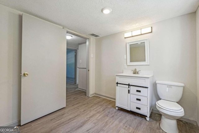 bathroom with vanity, toilet, wood-type flooring, and a textured ceiling