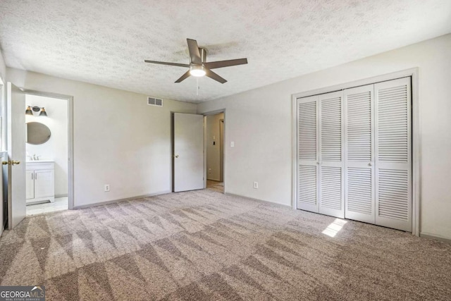 unfurnished bedroom featuring light carpet, ceiling fan, a textured ceiling, ensuite bathroom, and a closet