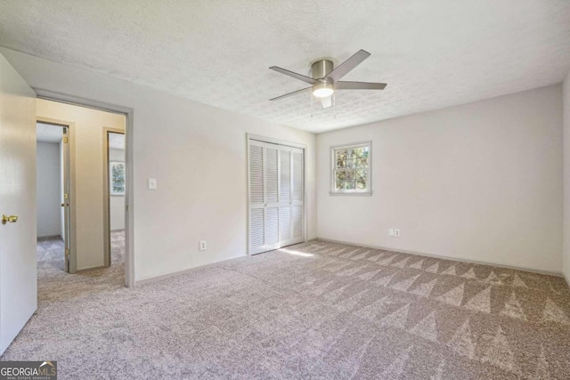 unfurnished bedroom featuring light carpet, a closet, a textured ceiling, and ceiling fan