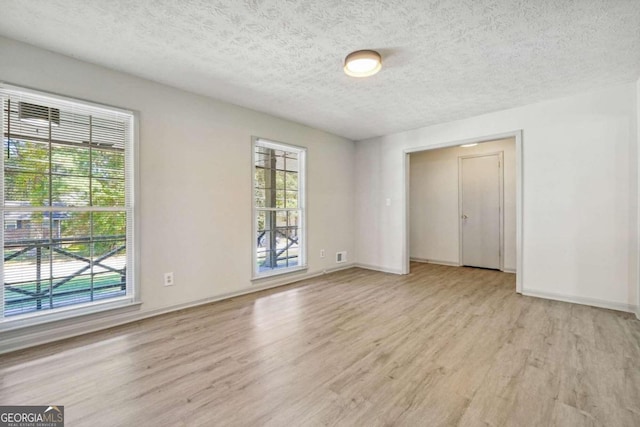 empty room with light hardwood / wood-style floors, a textured ceiling, and a wealth of natural light