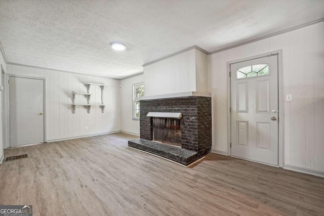 unfurnished living room featuring wood-type flooring, a textured ceiling, a fireplace, and ornamental molding