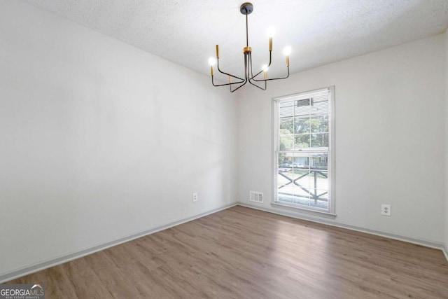 unfurnished room featuring a notable chandelier, a textured ceiling, and hardwood / wood-style flooring