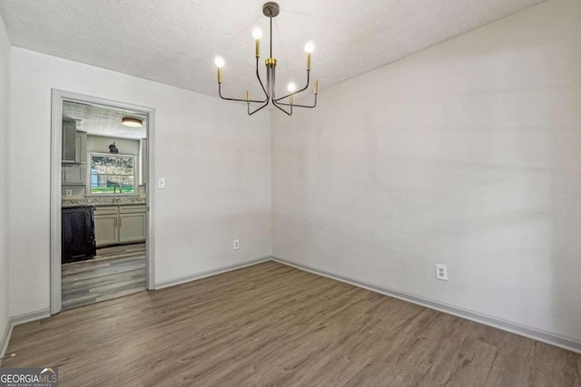 unfurnished dining area with hardwood / wood-style flooring, a textured ceiling, and an inviting chandelier