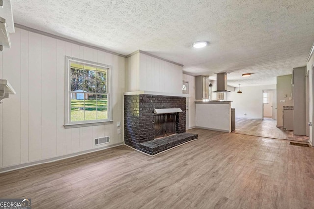 unfurnished living room featuring a fireplace, wooden walls, crown molding, light wood-type flooring, and a textured ceiling