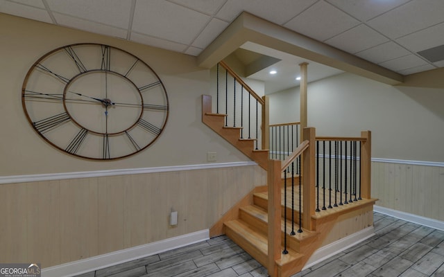 stairs with a drop ceiling, hardwood / wood-style flooring, and wood walls