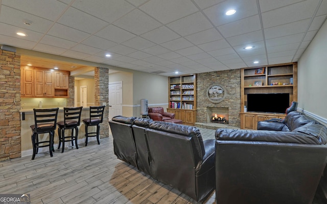 living room with light wood-type flooring, a fireplace, decorative columns, built in features, and a paneled ceiling