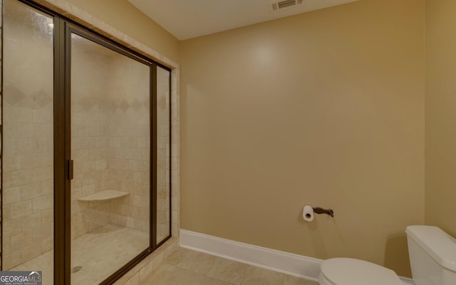 bathroom featuring toilet, a shower with shower door, and tile patterned flooring