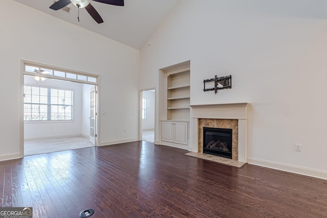 unfurnished living room featuring built in shelves, ceiling fan, wood-type flooring, and a tiled fireplace