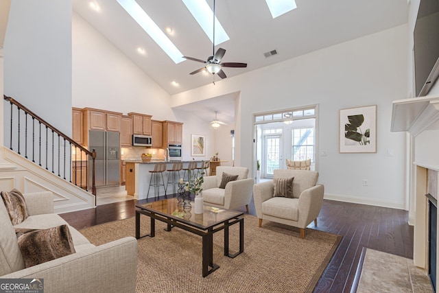 living room with ceiling fan, dark hardwood / wood-style flooring, a skylight, and high vaulted ceiling