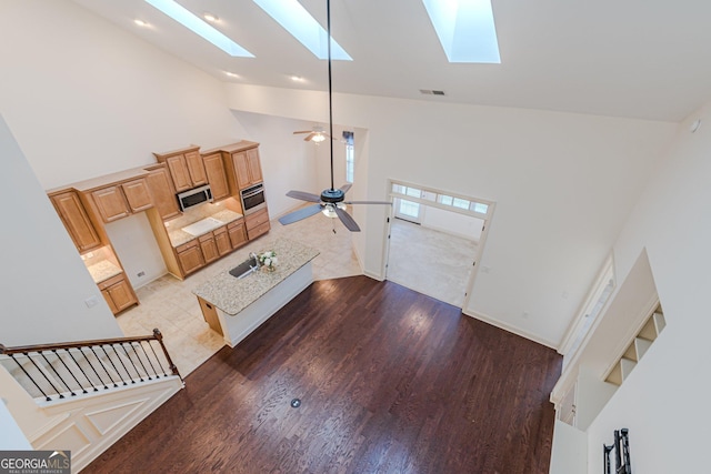 living room with hardwood / wood-style flooring, a skylight, high vaulted ceiling, and ceiling fan