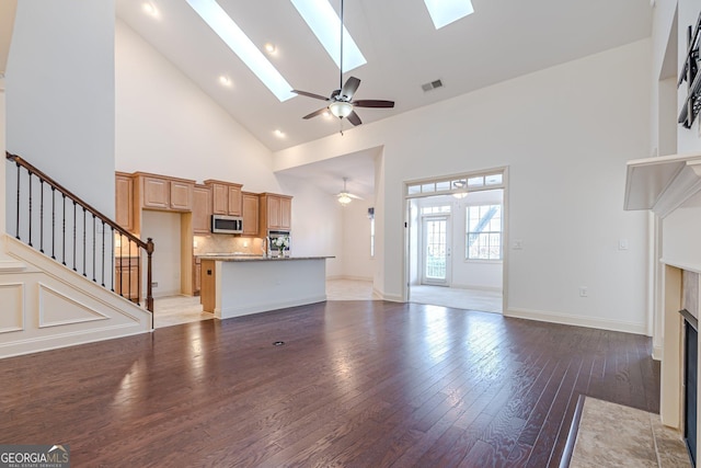 unfurnished living room with a tile fireplace, hardwood / wood-style floors, high vaulted ceiling, a skylight, and ceiling fan