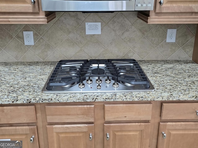 kitchen with backsplash, light stone countertops, and stainless steel gas cooktop