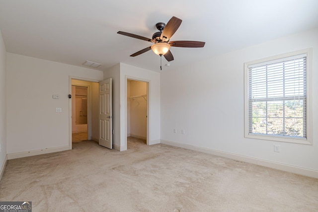 unfurnished bedroom with ceiling fan, light colored carpet, a spacious closet, and a closet