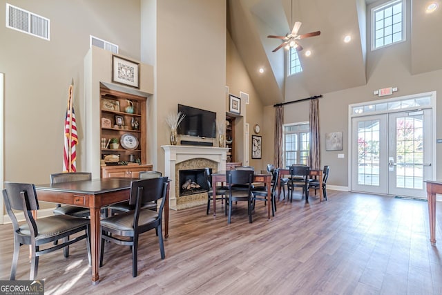 dining space with french doors, ceiling fan, a high end fireplace, light hardwood / wood-style floors, and a high ceiling