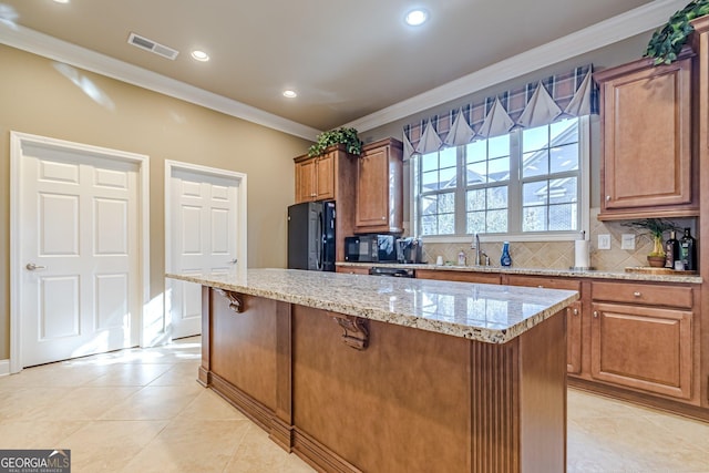 kitchen with crown molding, tasteful backsplash, light stone countertops, a kitchen island, and black fridge