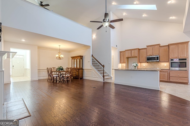 living room with ceiling fan with notable chandelier, high vaulted ceiling, a skylight, crown molding, and light hardwood / wood-style flooring