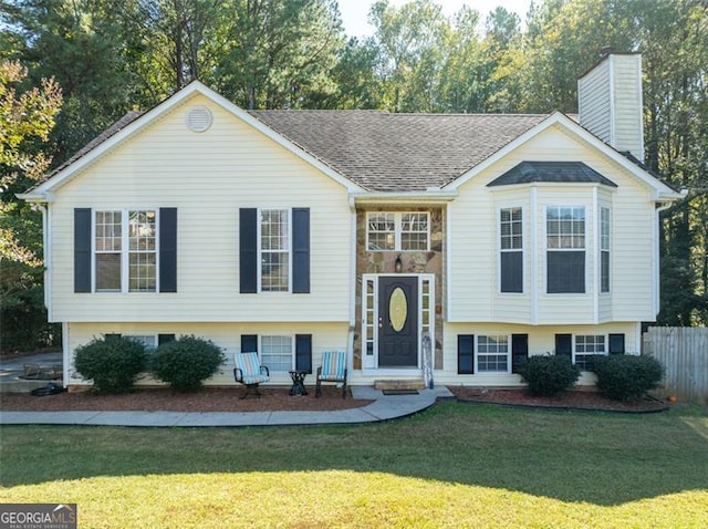 split foyer home featuring a chimney, fence, a shingled roof, and a front lawn