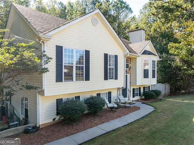 bi-level home featuring a chimney, a shingled roof, and a front lawn
