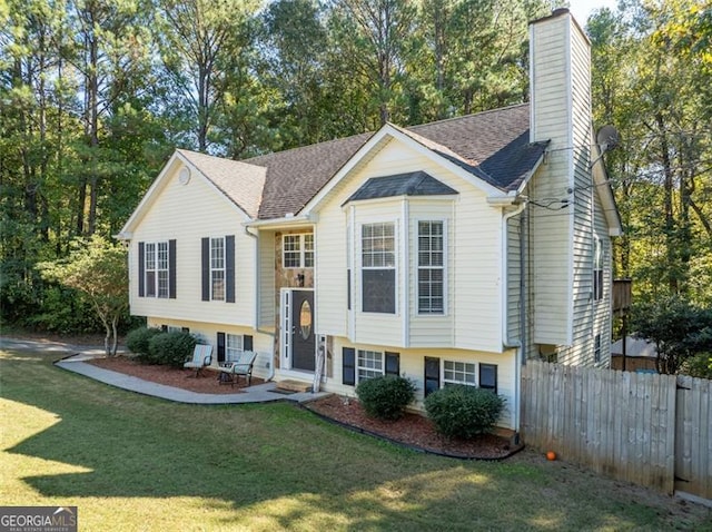 raised ranch with a chimney, fence, a front lawn, and roof with shingles