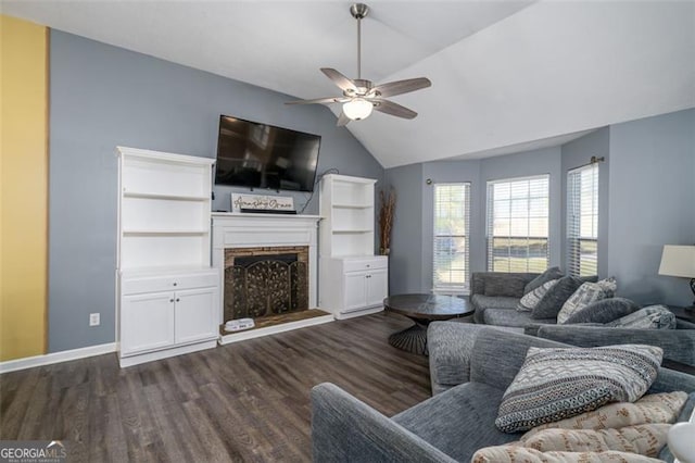living area with lofted ceiling, dark wood-style flooring, a fireplace with raised hearth, and a ceiling fan