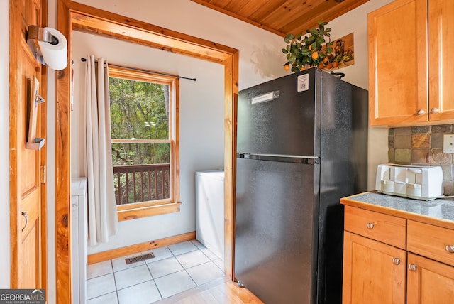 kitchen with backsplash, wooden ceiling, light tile patterned floors, and black fridge