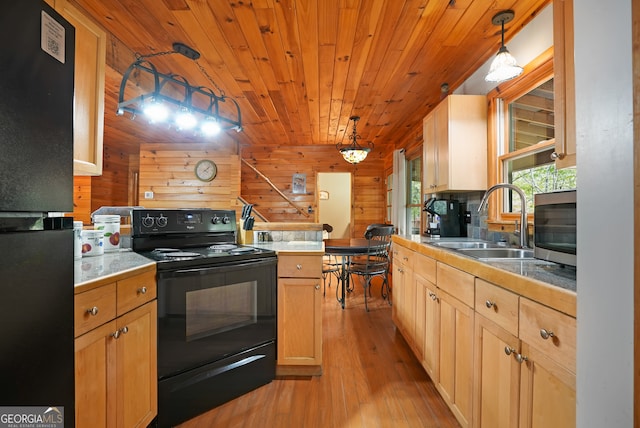 kitchen featuring light hardwood / wood-style flooring, black appliances, sink, pendant lighting, and wooden walls