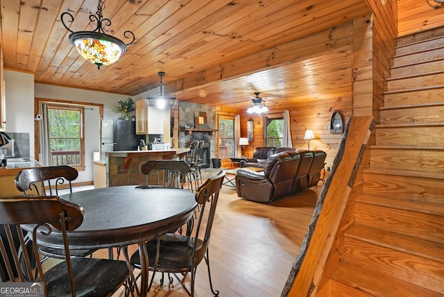 dining area featuring ceiling fan, wooden ceiling, light hardwood / wood-style flooring, a stone fireplace, and wooden walls