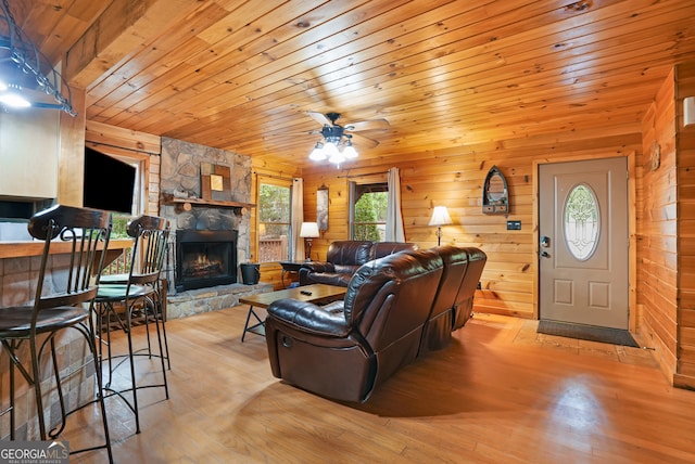 living room with wood walls, a fireplace, wood ceiling, light hardwood / wood-style floors, and ceiling fan