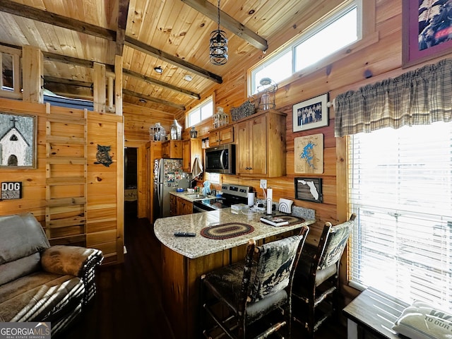 kitchen with vaulted ceiling with beams, wooden walls, hanging light fixtures, wooden ceiling, and appliances with stainless steel finishes