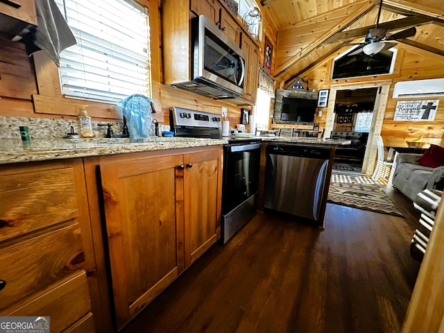 kitchen with vaulted ceiling with beams, dark hardwood / wood-style floors, light stone countertops, appliances with stainless steel finishes, and wood walls