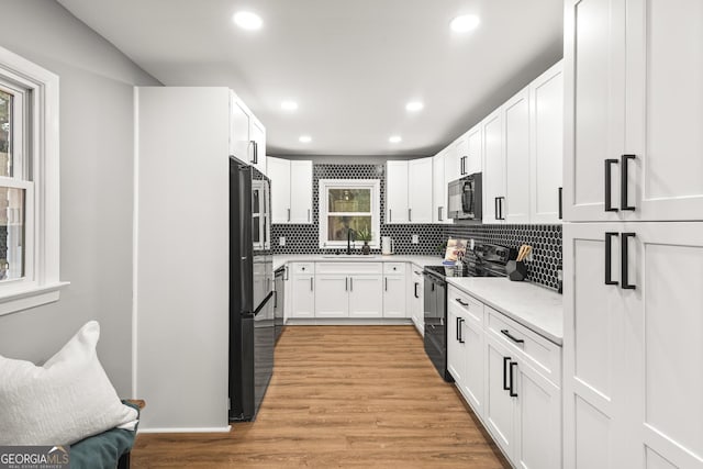 kitchen featuring sink, white cabinetry, light hardwood / wood-style flooring, decorative backsplash, and black appliances