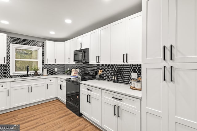 kitchen with sink, black appliances, light hardwood / wood-style flooring, white cabinets, and backsplash