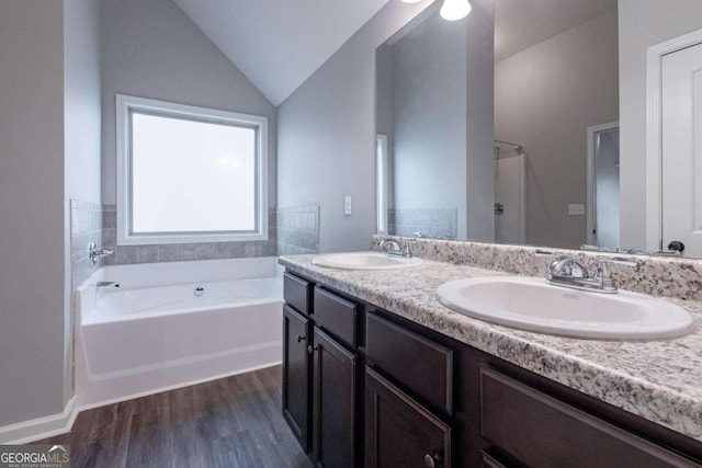 bathroom with vanity, hardwood / wood-style floors, vaulted ceiling, and a bathtub