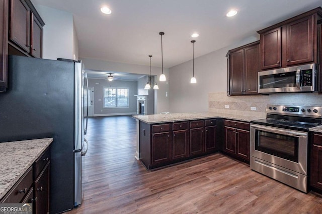 kitchen with appliances with stainless steel finishes, kitchen peninsula, hardwood / wood-style floors, and hanging light fixtures